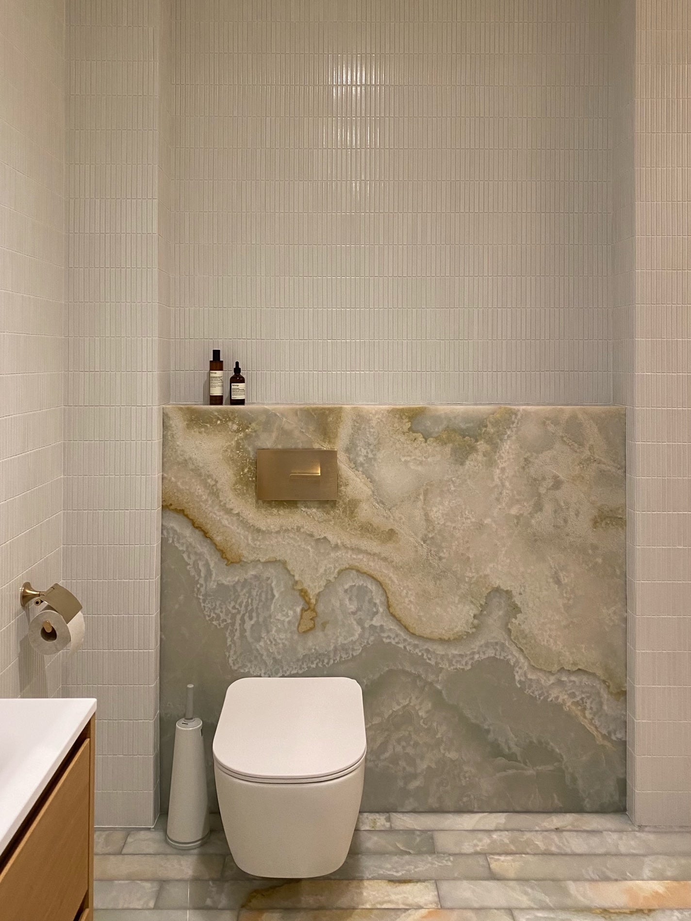 Yohen White tiled wall meeting a translucent stone panel in a private Latvian home.