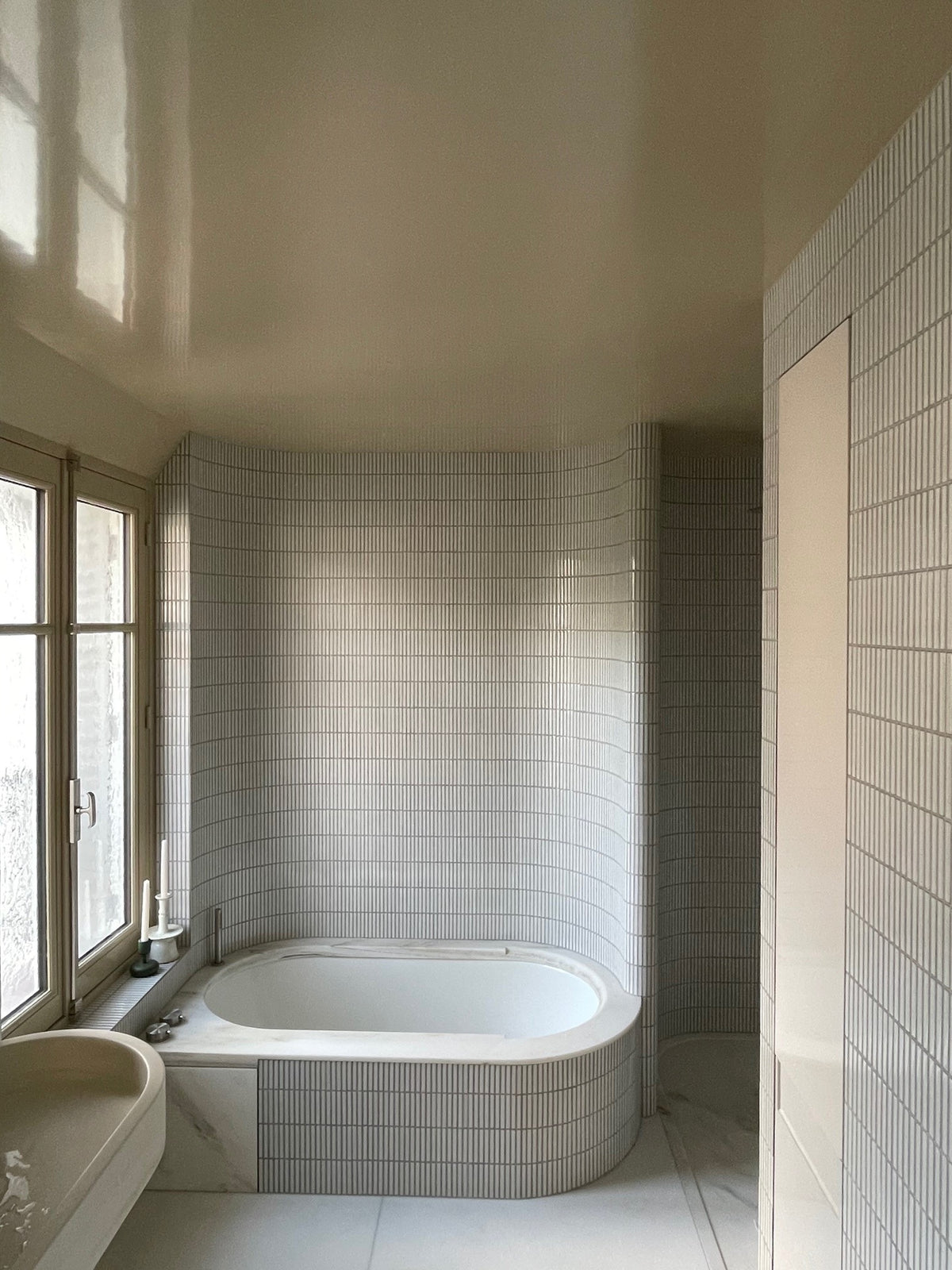 Curved bath wall finished in vertically laid Yohen Speckled White tiles.